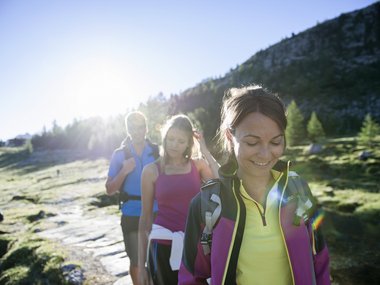 Three hikers on a sunny mountain trail with backpacks and sportswear